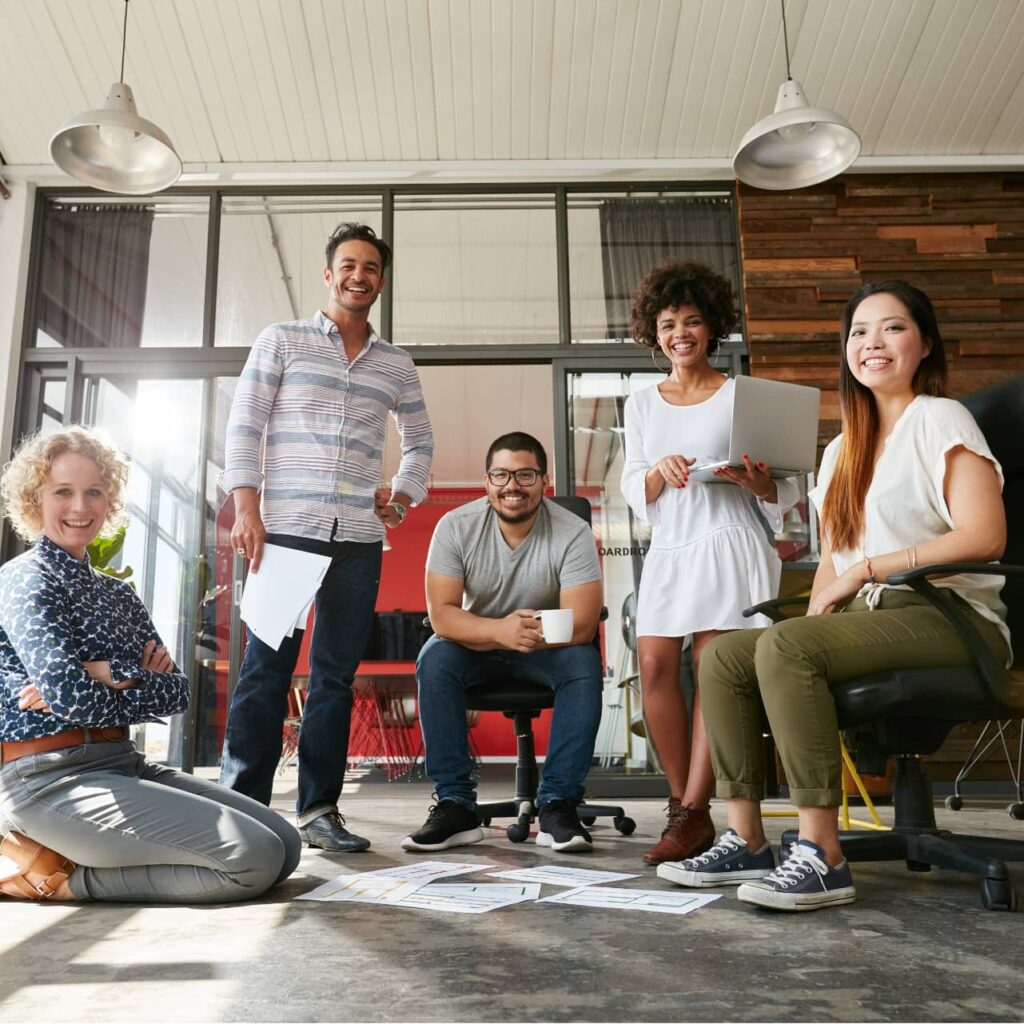 Five people in a modern office, smiling and posing around papers on the floor.